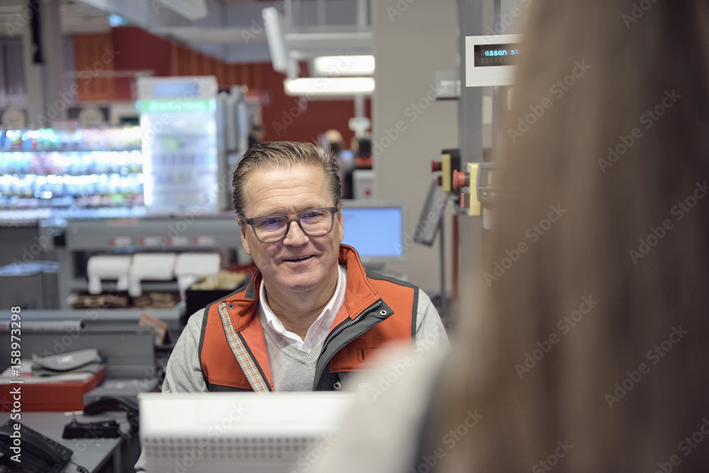 Smiling mature cashier looking at woman at checkout in supermarket Smiling mature cashier looking at woman at checkout in supermarket