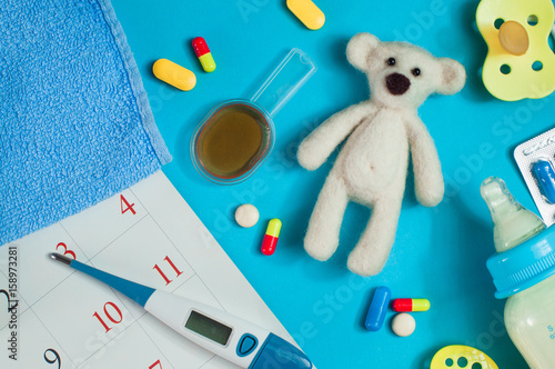 Pills, milk bottle and electronic thermometer near calendar page
