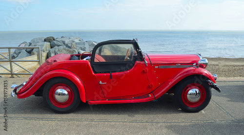  Classic  Red  Singer  Car  parked on seafront promenade with sea in background.