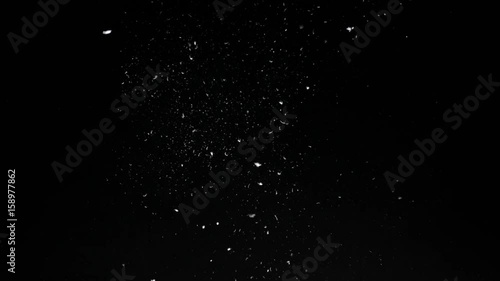 Coarse dirt elements and feathers blown upwards then slowly settling down black background