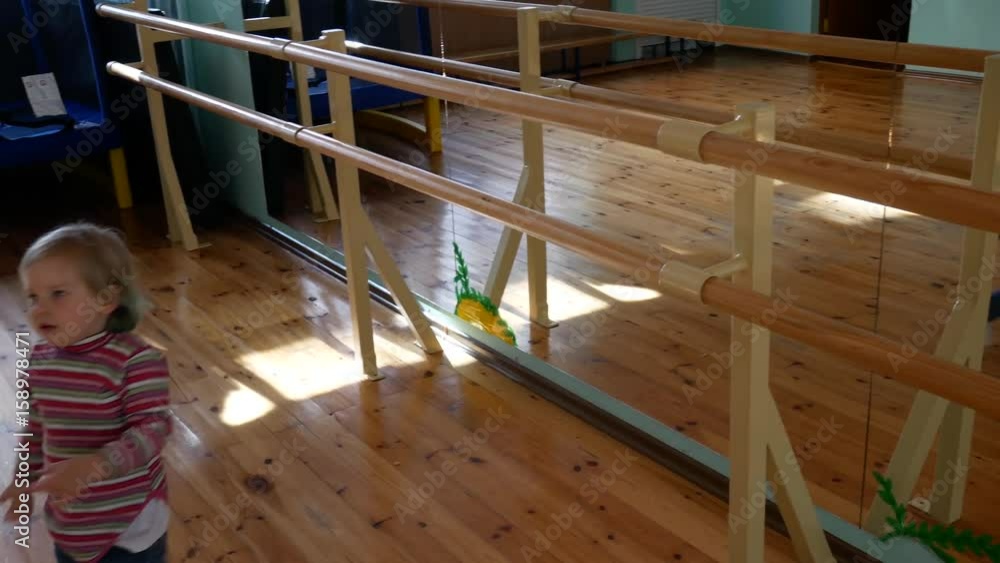 The child is playing in the gym. The blond girl is hanging, pulling at the gymnastic outfit. The child is playing in the gym. The blond girl is hanging, pulling at the gymnastic outfit.