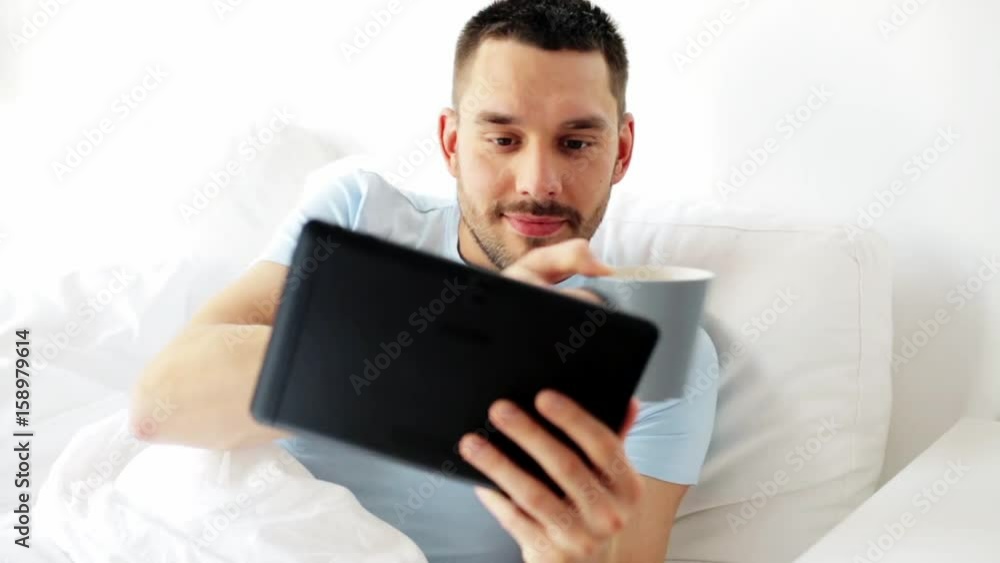 man with tablet pc drinking coffee in bed at home man with tablet pc drinking coffee in bed at home