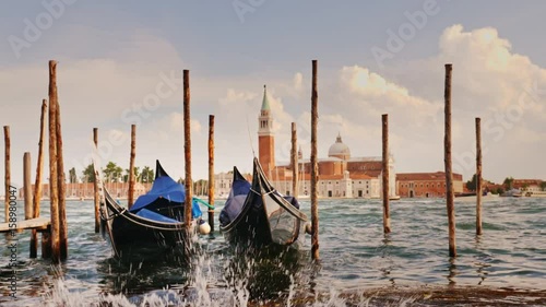 Two gondolas at the pier against the backdrop of the coastline of Venice, Italy. In the foreground, water splashes, slow motion 4K video
