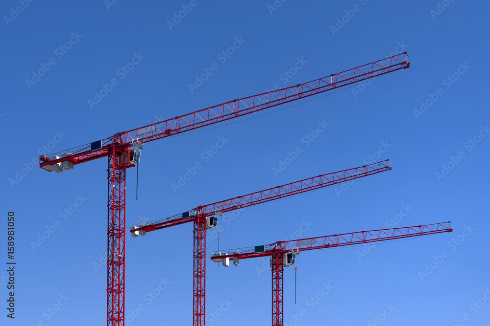 Three red industrial construction tower cranes against blue sky Three red industrial construction tower cranes against blue sky