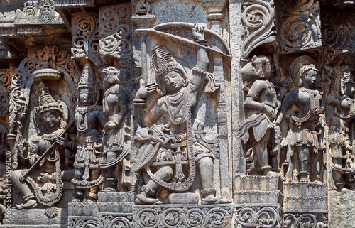 Ancient soldier with bow and arrow on the Hindu temple walls with friezes that consist of patterns, vedic scenes, mythical beasts and gods. 12th centur Hoysaleshwara temple in Halebidu, India.