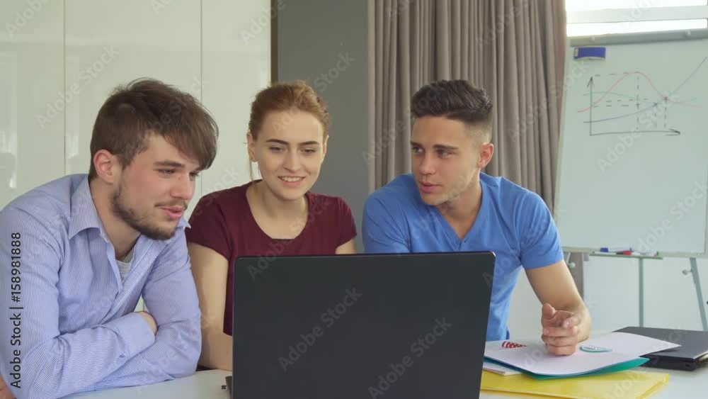 Three young people discussing something on laptop at the office. Handsome brunette guy pointing marker on the screen. Pretty redhead girl sitting between two caucasian men. Attractive bearded man Three young people discussing something on laptop at the office. Handsome brunette guy pointing marker on the screen. Pretty redhead girl sitting between two caucasian men. Attractive bearded man