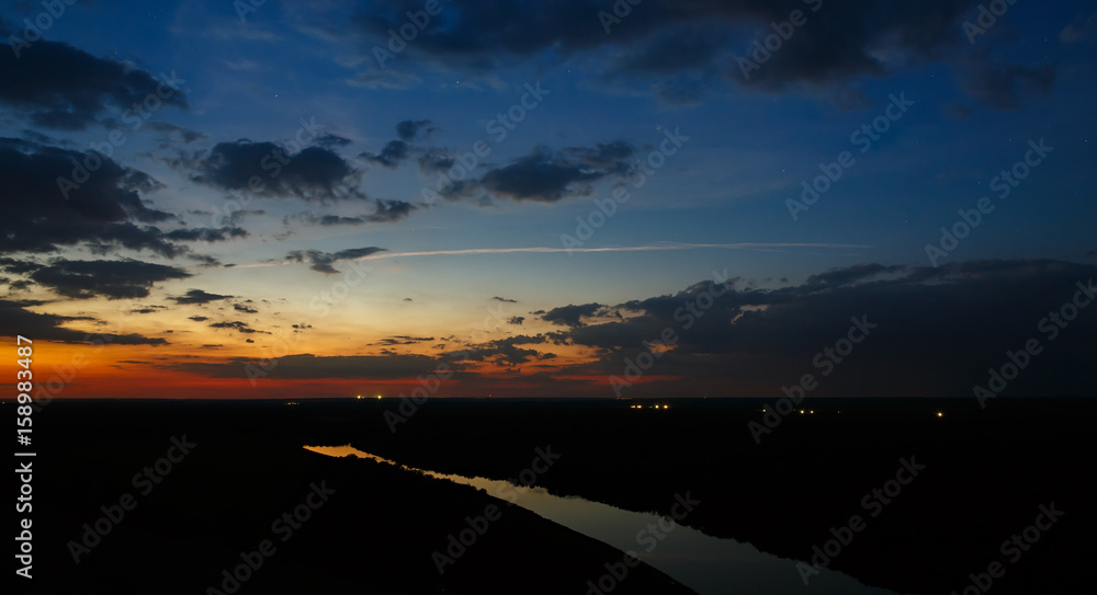 Starry sky with clouds over the river after sunset.