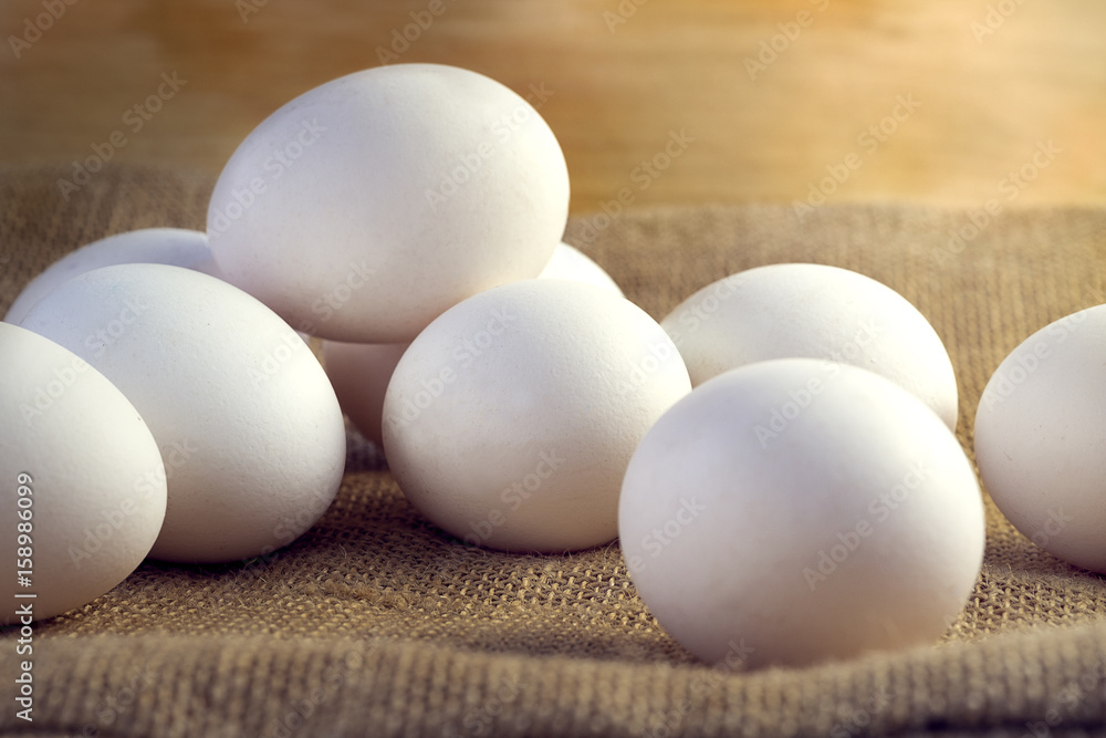 White chicken eggs wrapped in burlap next to a basket on a wooden table White chicken eggs wrapped in burlap next to a basket on a wooden table