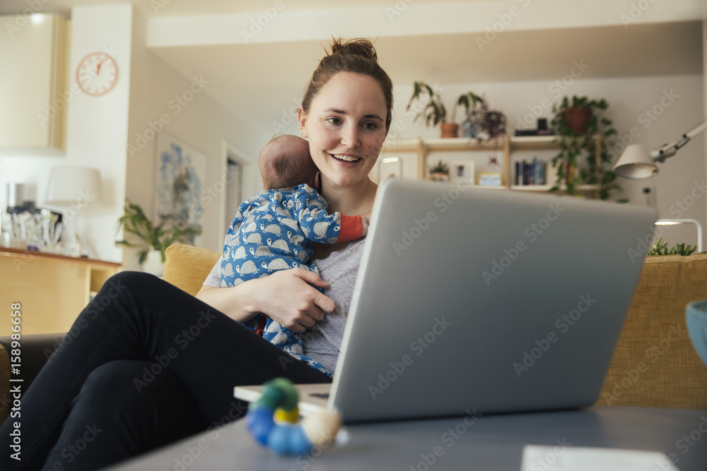 Mother using laptop and holding her newborn baby at home Mother using laptop and holding her newborn baby at home
