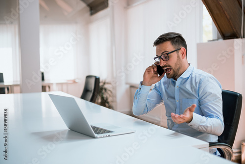 Angry businessman talking on the phone in office photo