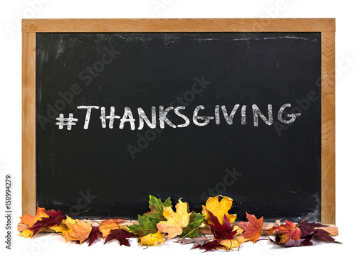 Hashtag Thanksgiving written in white chalk on a black chalkboard decorated with autumn fall leaves isolated on white