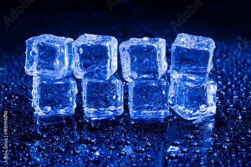 Ice cubes in blue light on black wet table.