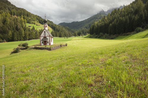 St. Johann little church among a wide green meadow in St. Magdalena , Val di Funes