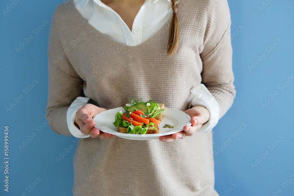 Healthy sandwich in plate, in female hands, with avocado, tomato, and salad, on toast Healthy sandwich in plate, in female hands, with avocado, tomato, and salad, on toast