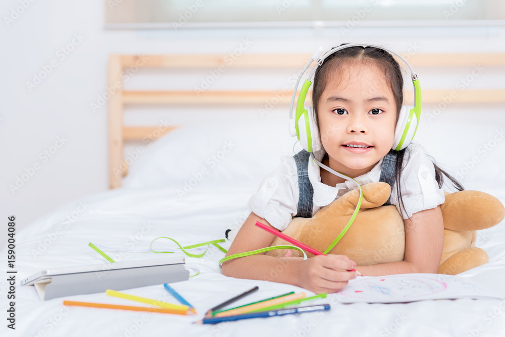 Cute asian little girl doing homework,writing with colourful pencils on bed at home. Elegant design for kid playing, preschool learning and creative art education concept. Cute asian little girl doing homework,writing with colourful pencils on bed at home. Elegant design for kid playing, preschool learning and creative art education concept.