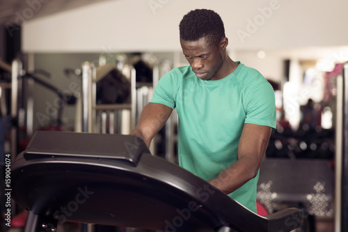 black man manipulates a running machine at the gym