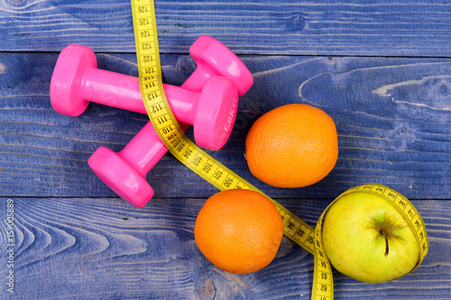 fitness concept, dumbbells weight with measuring tape, orange and apple