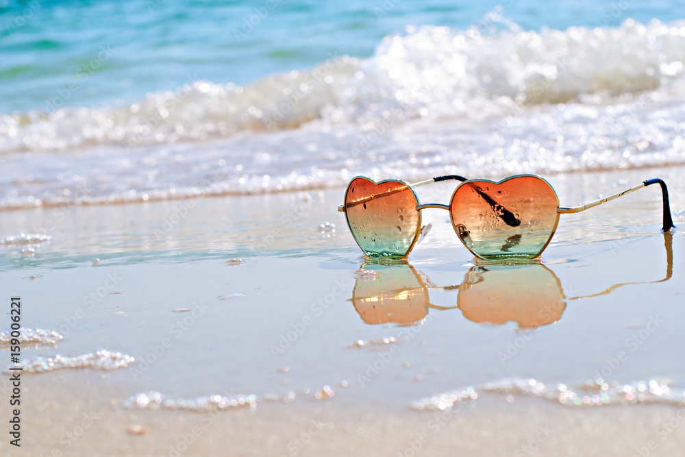 Heart-shaped sunglasses on the wet sand, beach at the seaside. Travel and vacation concept