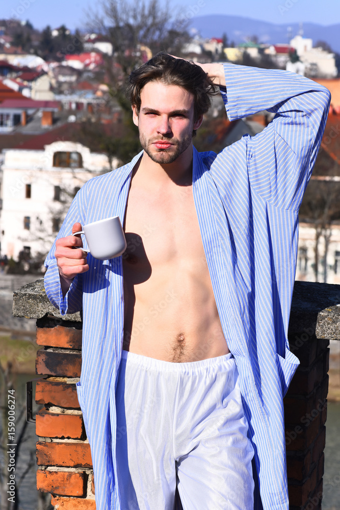 Caucasian macho in blue striped pajamas holding cup - obrazy, fototapety, plakaty 