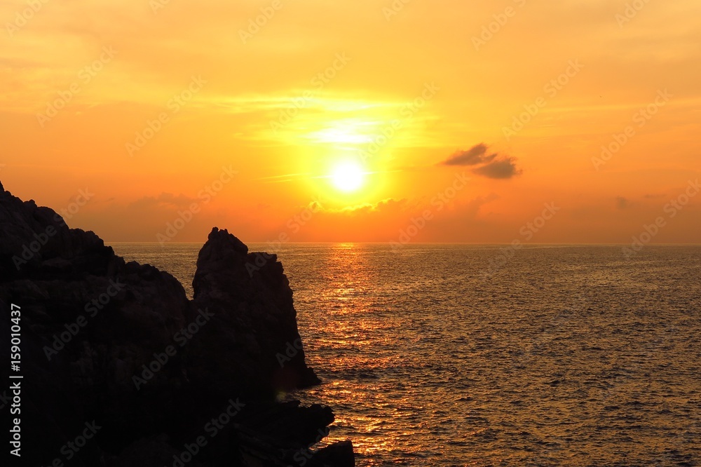 sunrise sunset over sea with rocky coast in foreground