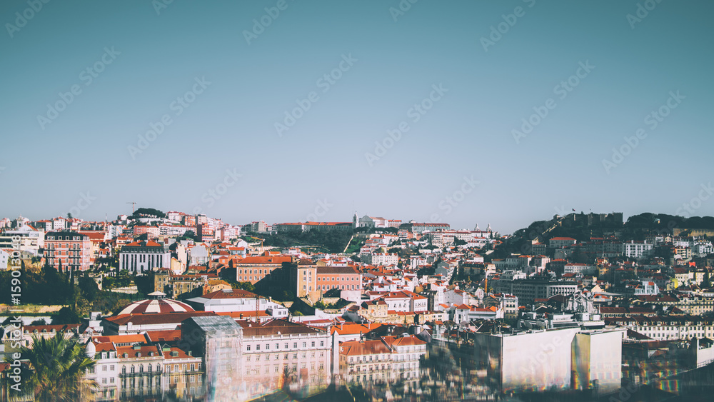 Wide beautiful panoramic view from high point of central  Lisbon district on sunny summer day: multiple houses with red roofs, castle in distance, clear sky and reflections with aberrations in bottom