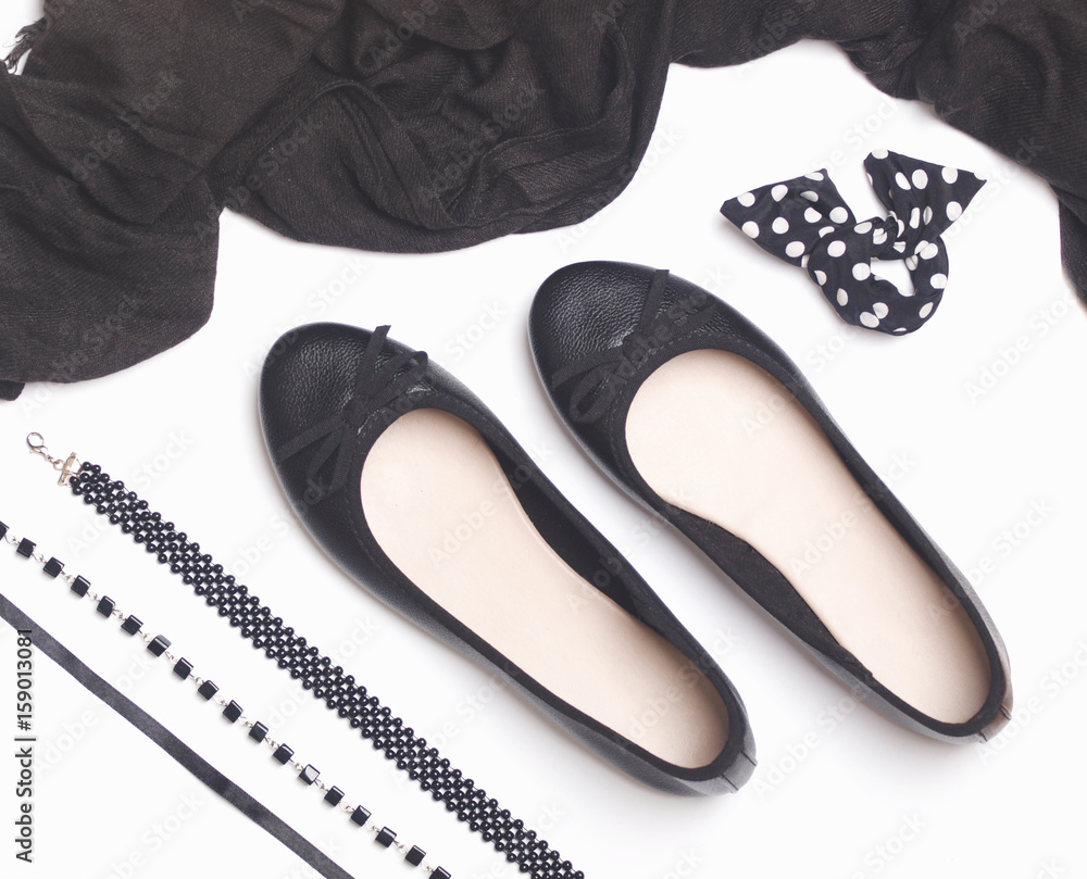 Obraz premium Black faux leather ballet flats with black accessories like scarf, bracelet and necklaces on white background. Flat lay. Top view.