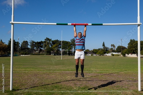 Full length of rugby player hanging on goal post at field
