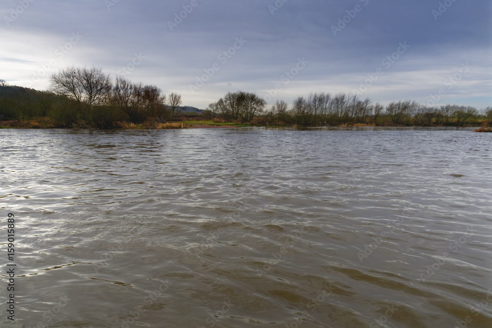 Looking across the fast flowing River Trent to a tree lined riverbank on a windy, dark, cloudy winter's day Looking across the fast flowing River Trent to a tree lined riverbank on a windy, dark, cloudy winter's day