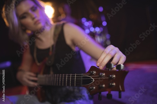 Singer adjusting tuning peg of guitar in nightclub