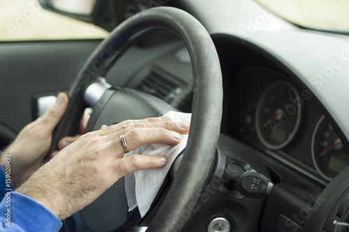 Dłoń mężczyzny wyciera kierownice samochodu białą szmatką. © Tomasz