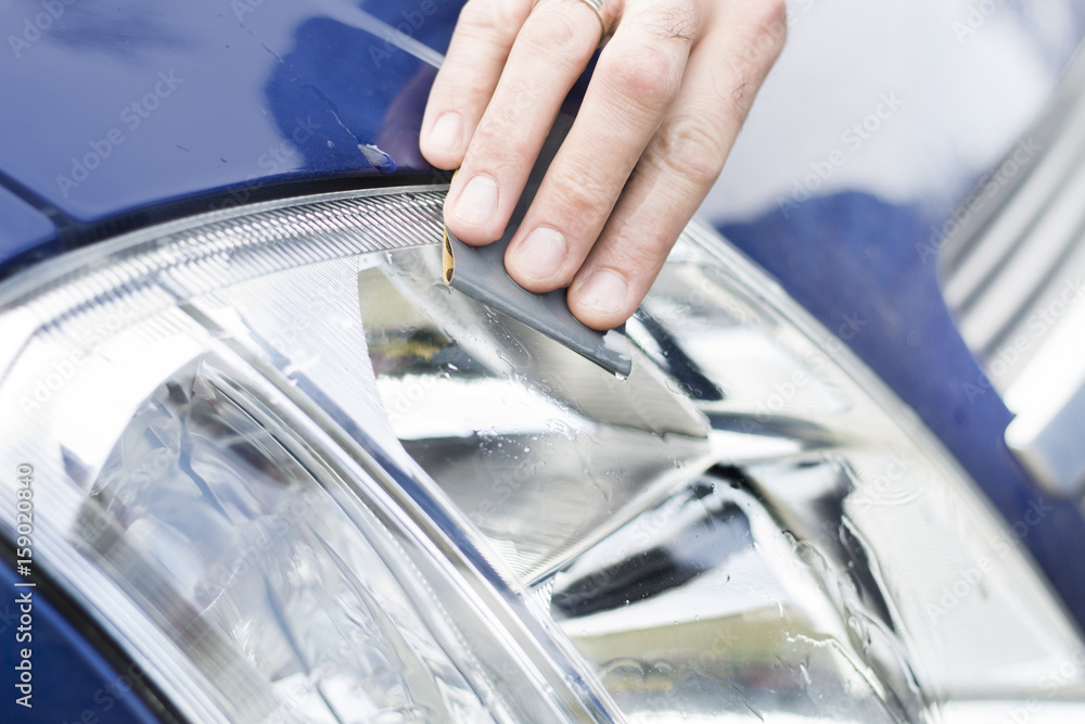 Dłoń mechanika samochodowego poleruje papierem ściernym i wodą zmatowiałe szkło reflektora. Auto detailing. Odnawianie szkła reflektora. Polerowanie papierem ściernym i wodą.
