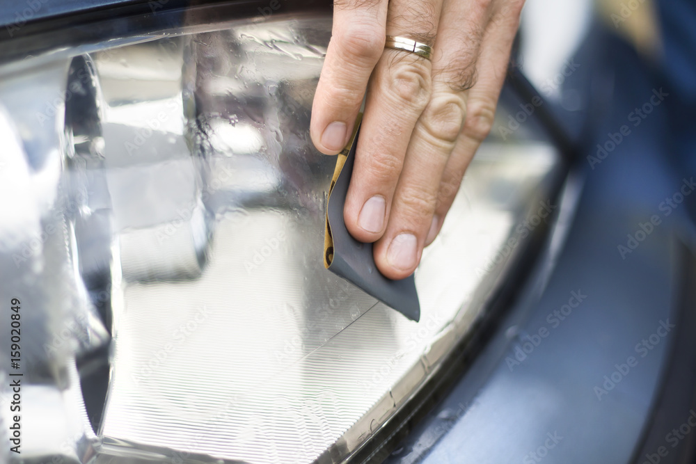 Dłoń mechanika samochodowego poleruje papierem ściernym i wodą zmatowiałe szkło reflektora. Auto detailing. Odnawianie szkła reflektora. Polerowanie papierem ściernym i wodą.