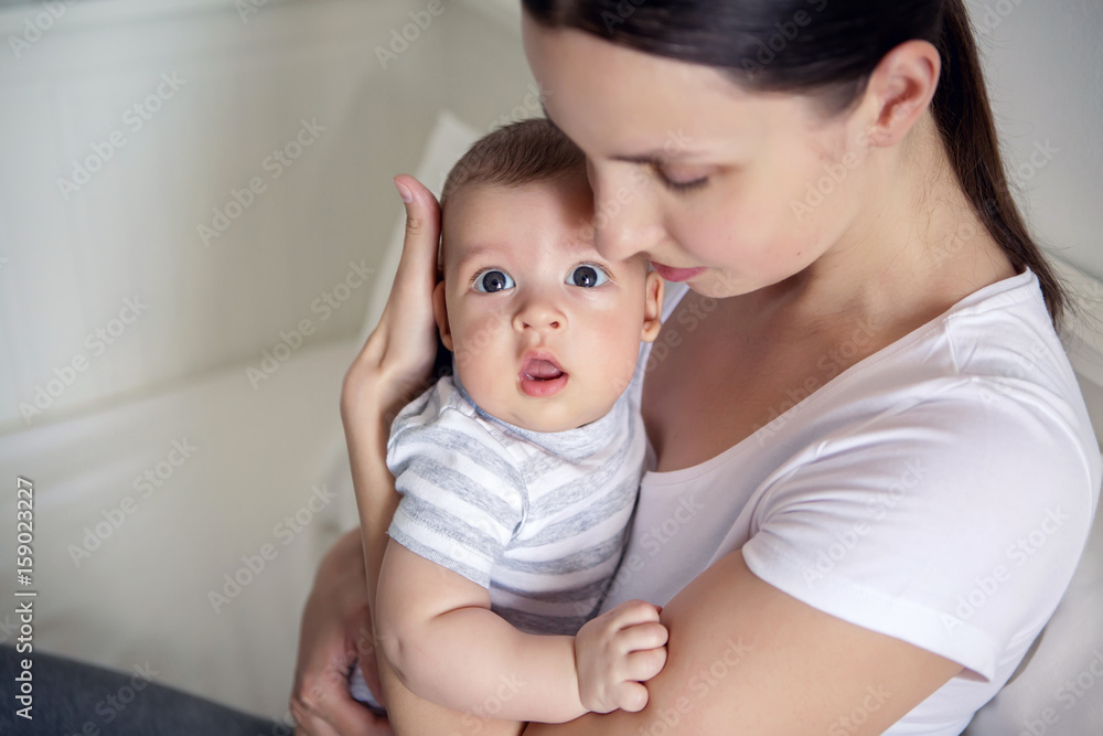 mother with her newborn son in hands sitting on a big white bed mother with her newborn son in hands sitting on a big white bed