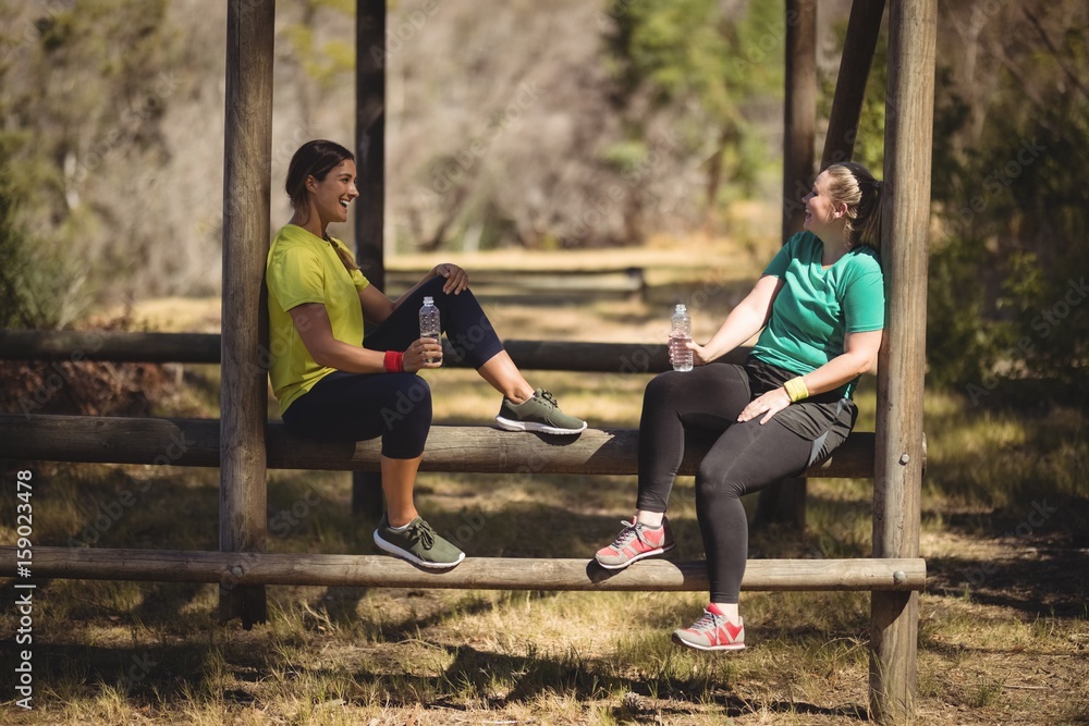 Happy friends relaxing on obstacle during obstacle course Happy friends relaxing on obstacle during obstacle course