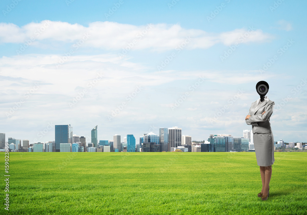 Camera headed woman standing on green grass against modern cityscape Camera headed woman standing on green grass against modern cityscape