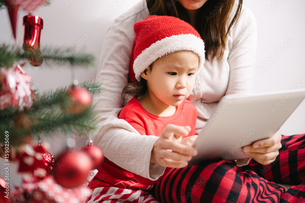Toddler girl and her mother using digital PC by christmas tree Toddler girl and her mother using digital PC by christmas tree