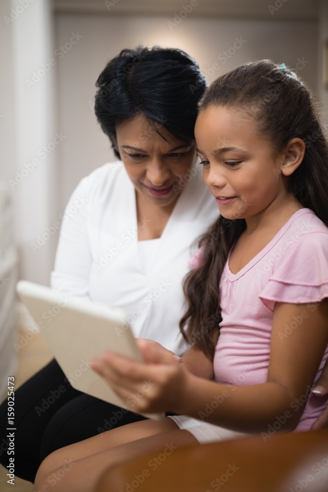 Girl using digital tablet while sitting with grandmother Girl using digital tablet while sitting with grandmother