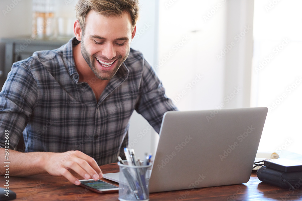 Happy young adult caucasian man smiling joyfully while looking at his phone, reading his latest messages to catch up with his social media as a way of procrastinating. Happy young adult caucasian man smiling joyfully while looking at his phone, reading his latest messages to catch up with his social media as a way of procrastinating.