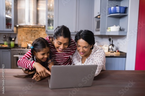 Happy multi-generation family using laptop in kitchen