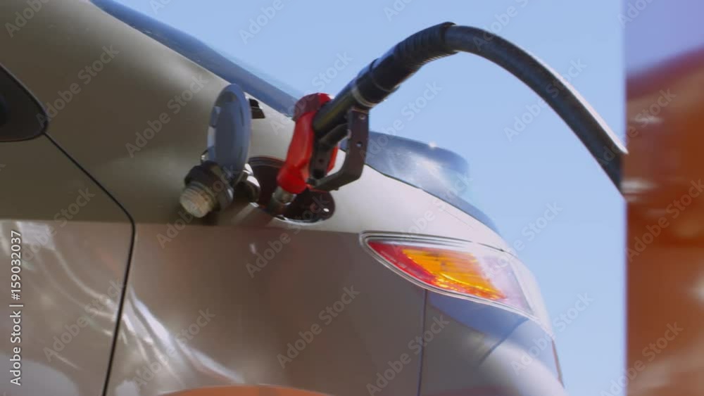 Tracking shot of opened car tank with fuel nozzle inserted into it at gas station Tracking shot of opened car tank with fuel nozzle inserted into it at gas station