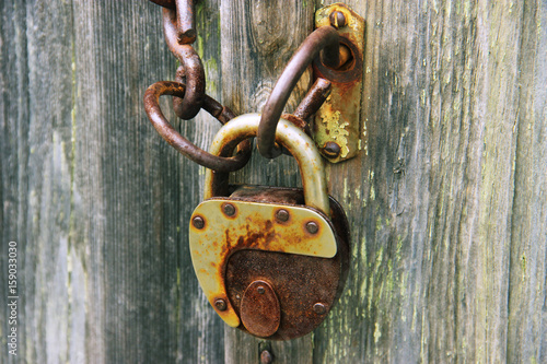 On the old wooden door, installed a rusty padlock. Wooden background.