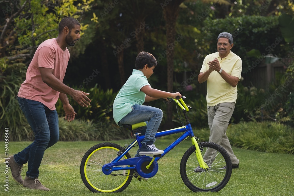 Fototapeta premium Father and grandfather motivating boy while riding bicycle