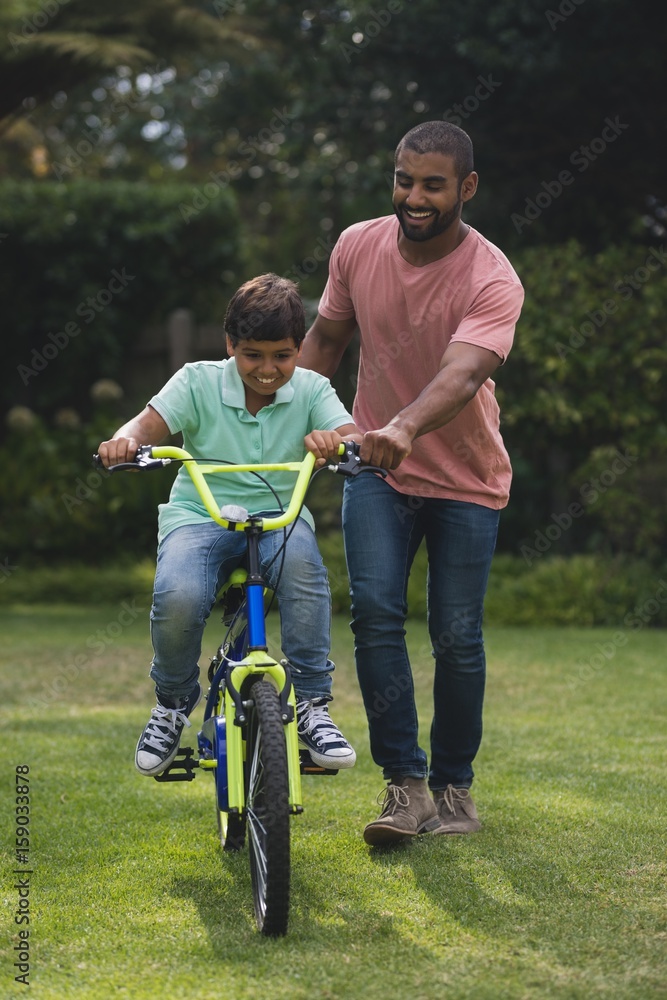 Obraz premium Father assisting son while riding bicycle