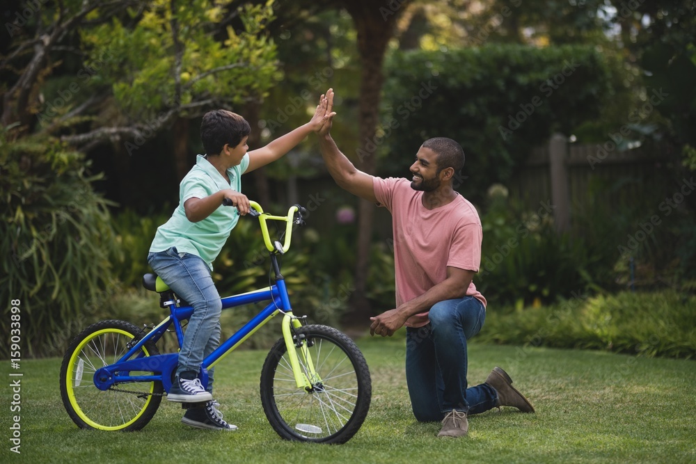 Boy giving high five to father while riding bicycle