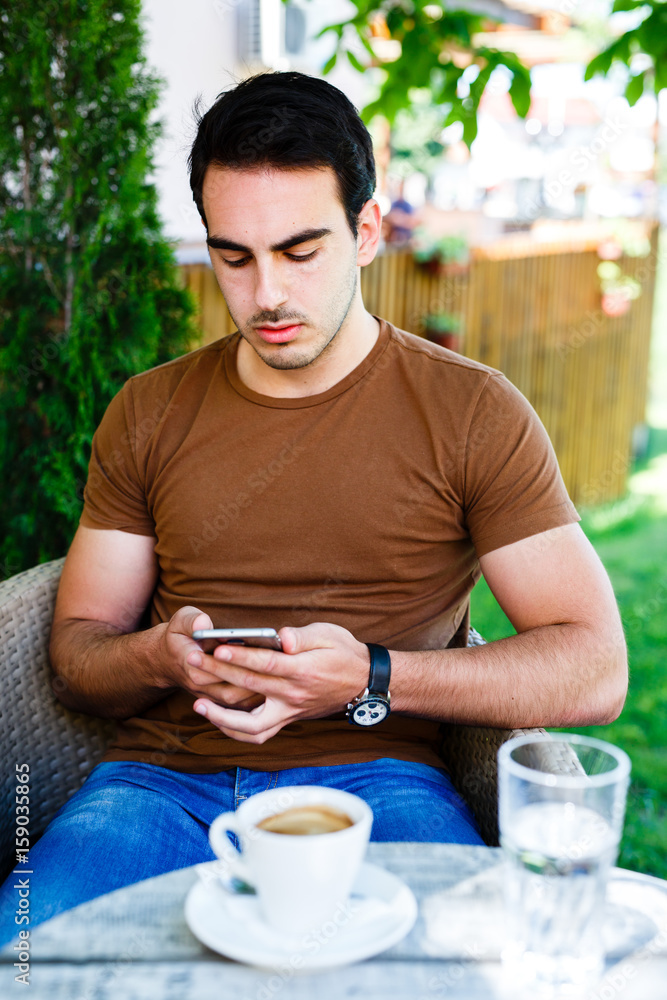 Young man sitting in caffe and typing on phone Young man sitting in caffe and typing on phone