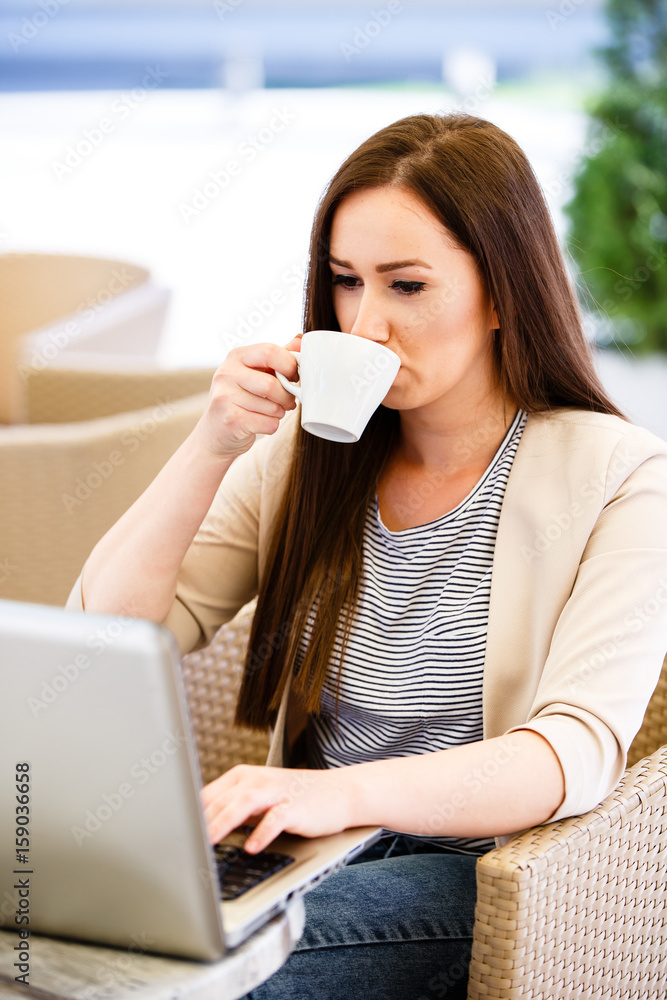 Modern woman in caffe drinking coffee and typing on laptop Modern woman in caffe drinking coffee and typing on laptop