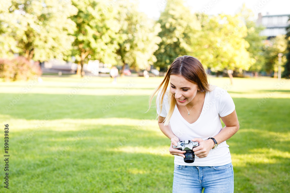 Cute girl in park smiling while taking photographs with her camera Cute girl in park smiling while taking photographs with her camera