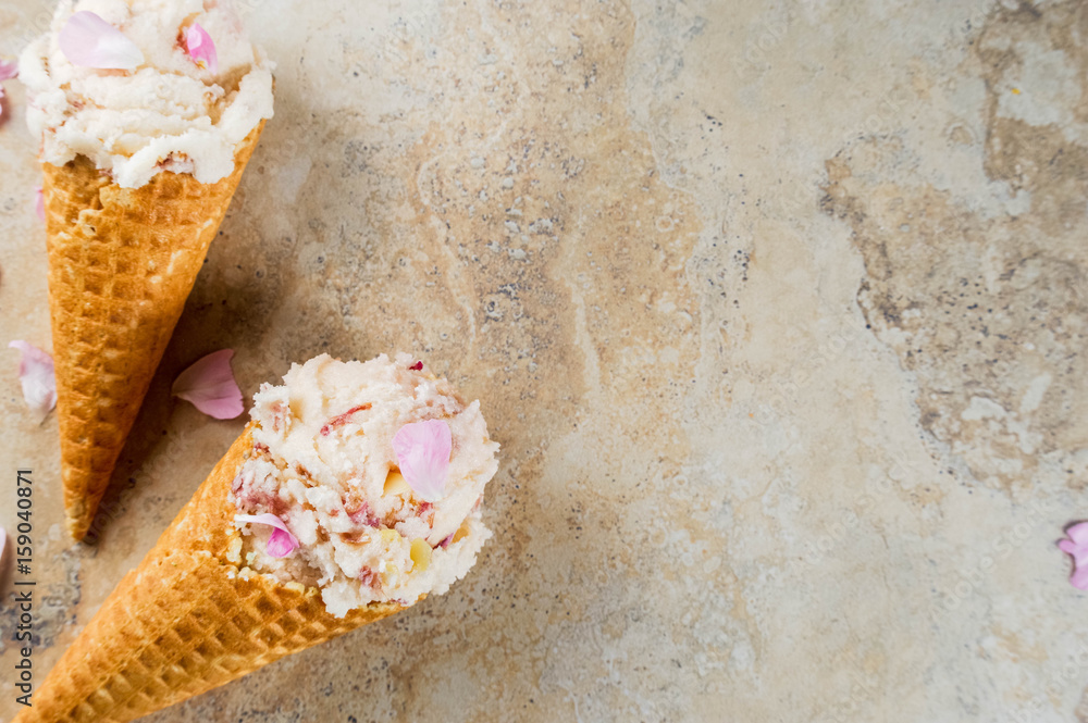 Summer refreshing desserts. Vegan diet food. Ice cream with rose petals and slices of almond, in classic waffle ice cream cones, on a beige light concrete table. Copy space top view Summer refreshing desserts. Vegan diet food. Ice cream with rose petals and slices of almond, in classic waffle ice cream cones, on a beige light concrete table. Copy space top view