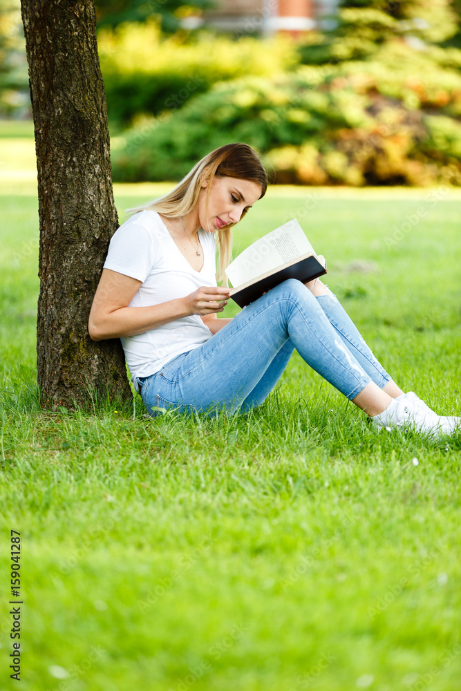 Modern student sitting in park under the tree and reading the book Modern student sitting in park under the tree and reading the book
