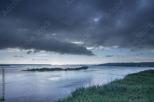 Very cloudy weather. Black clouds over the river. The edge of the river bank.